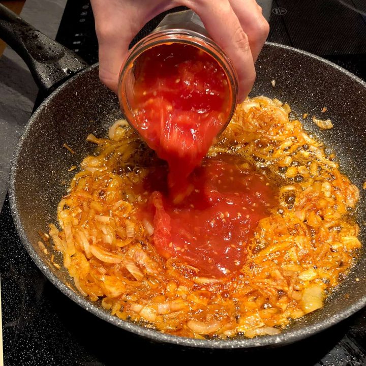 pouring chopped tomatoes into the pan