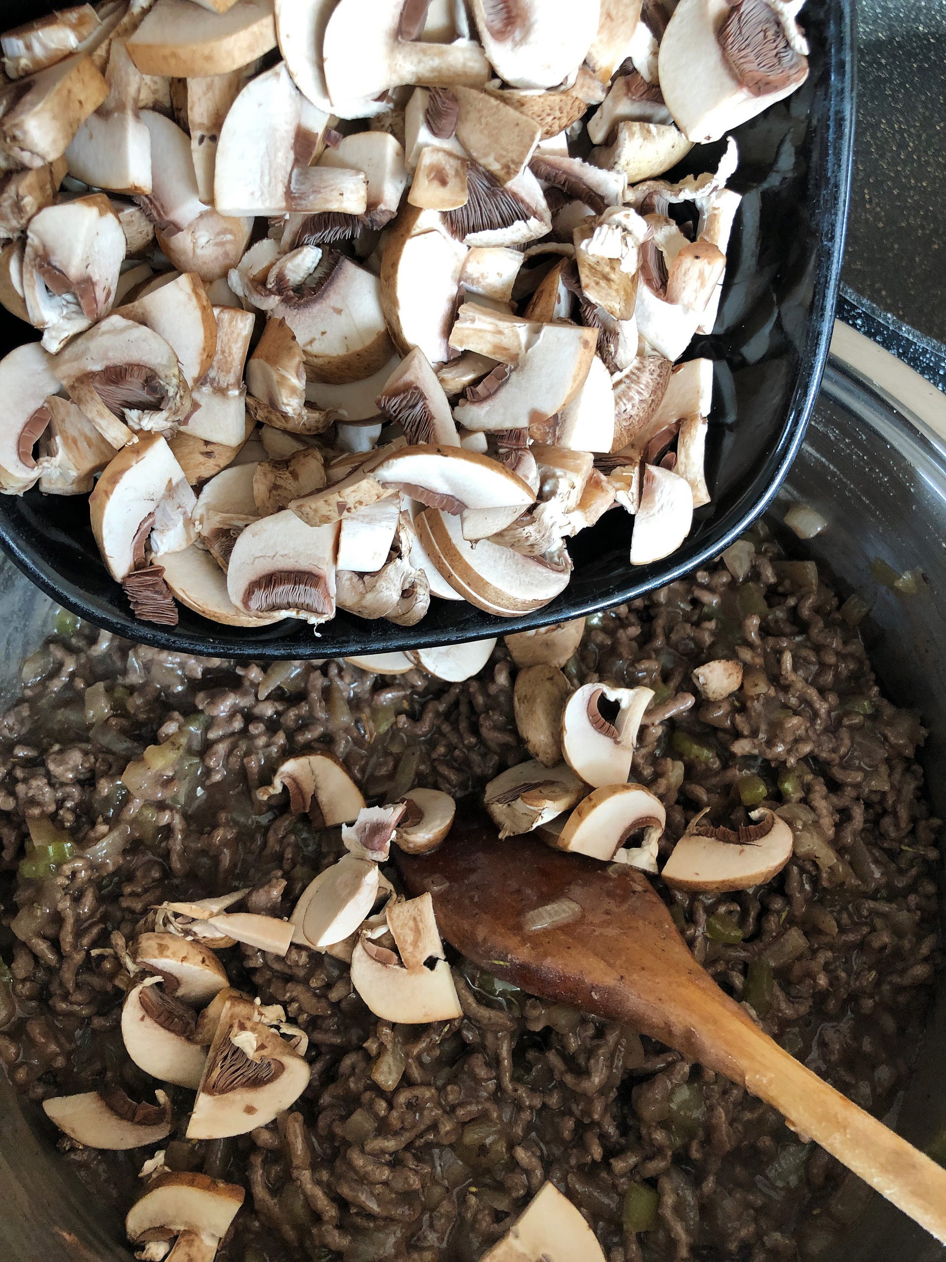 Adding sliced chestnut mushrooms into a pan with minced beef