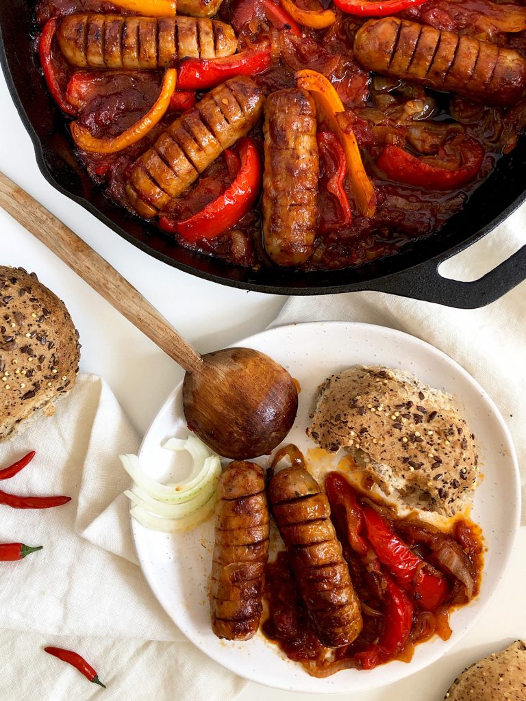 Two sausages with sauce and bell peppers served on a plate.