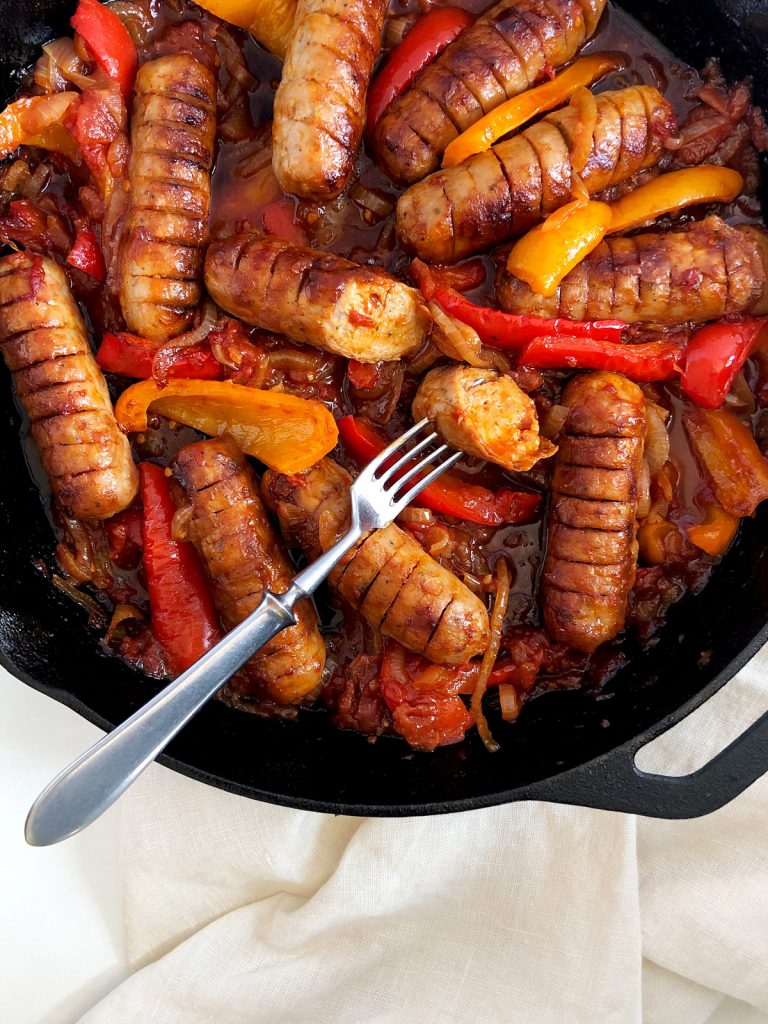 Juicy sausage casserole with sauce and belle peppers in a cast iron pan.