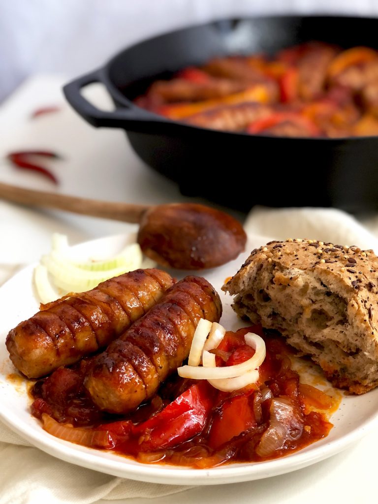 Two sausages served with a sauce and seeded bun on a plate.