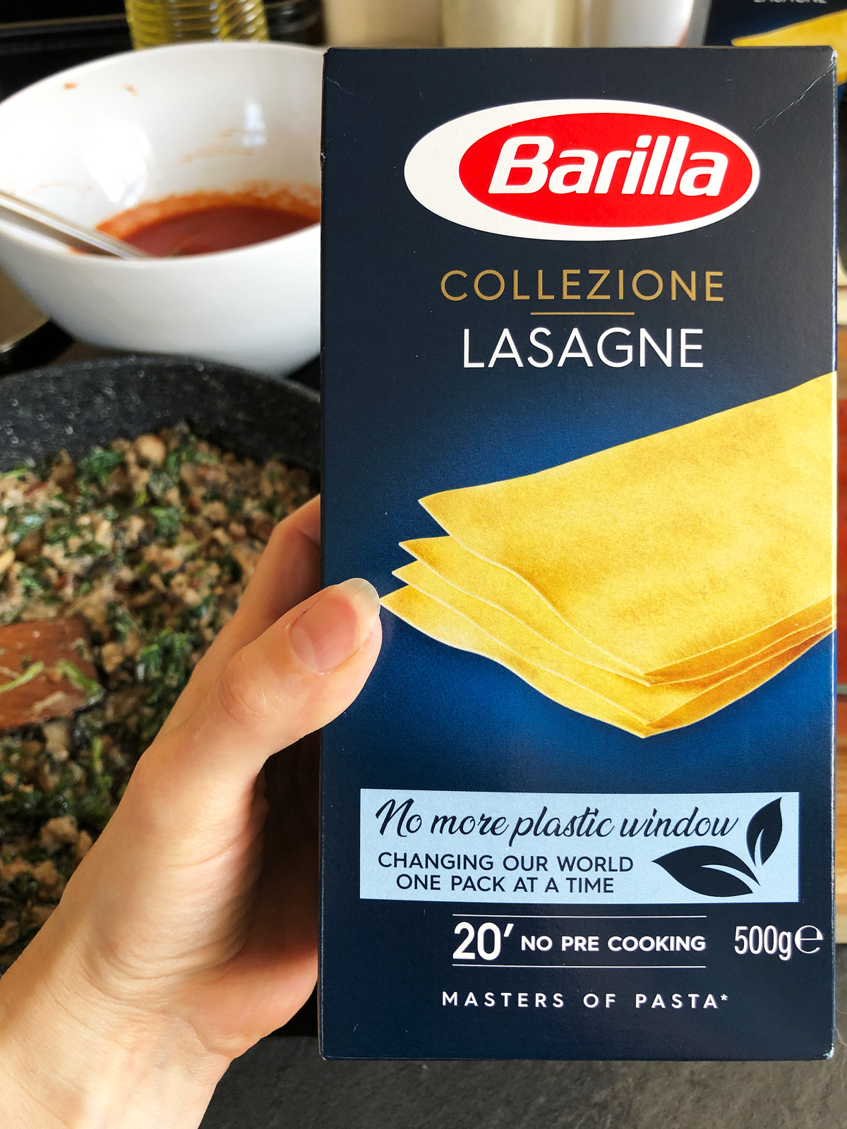 A hand holding Barilla lasagne in a blue packaging.
