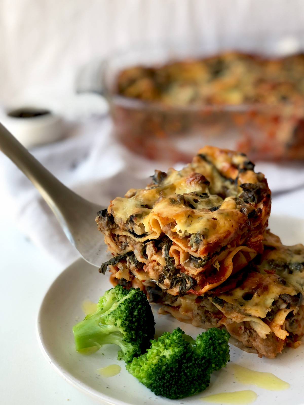 A plate with a serving of Mary Berry Express Lasagne with blanched broccoli.