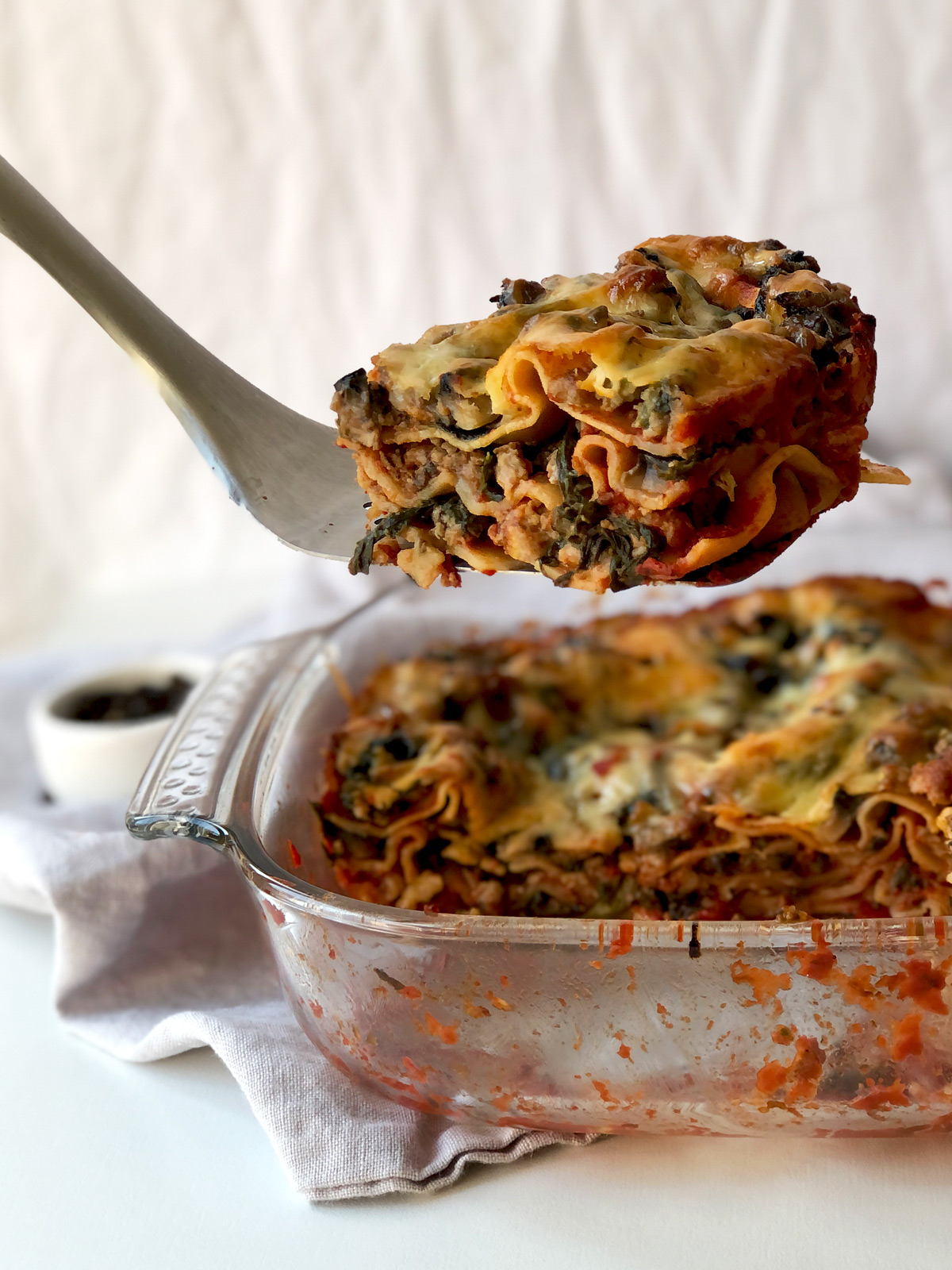 Serving of sausage meat, spinach and mushroom lasagne on a turning spatulla.