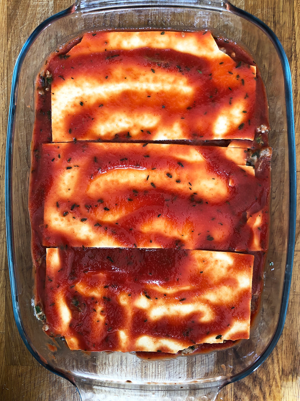 Assembling lasagne - dried lasagne sheets covered with tomato sauce in a glass oven dish.
