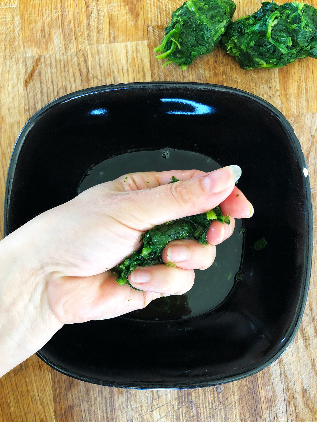 A hand holding defrosted spinach, sqeezing excess water to the bowl.