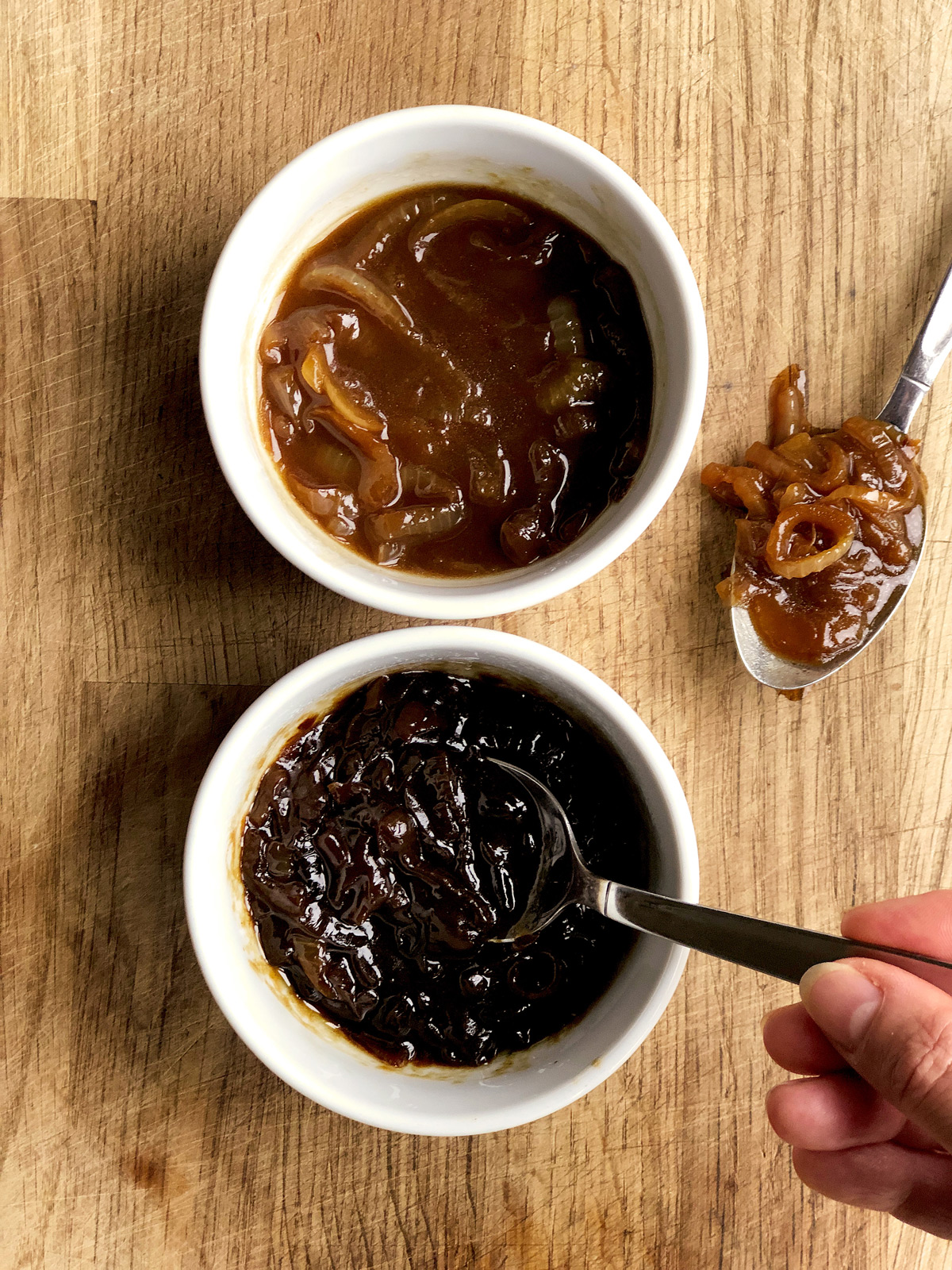 Two samples of onion gravy in small white bowls with two teaspoons.