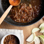 Brown and saucy onion gravy in a black frying pan; sliced onion and a small portion of the gravy in a white bowl.