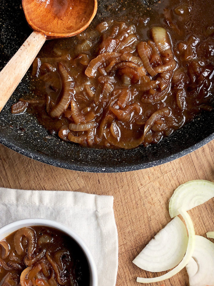 Brown and saucy onion gravy in a black frying pan; sliced onion and a small portion of the gravy in a white bowl.