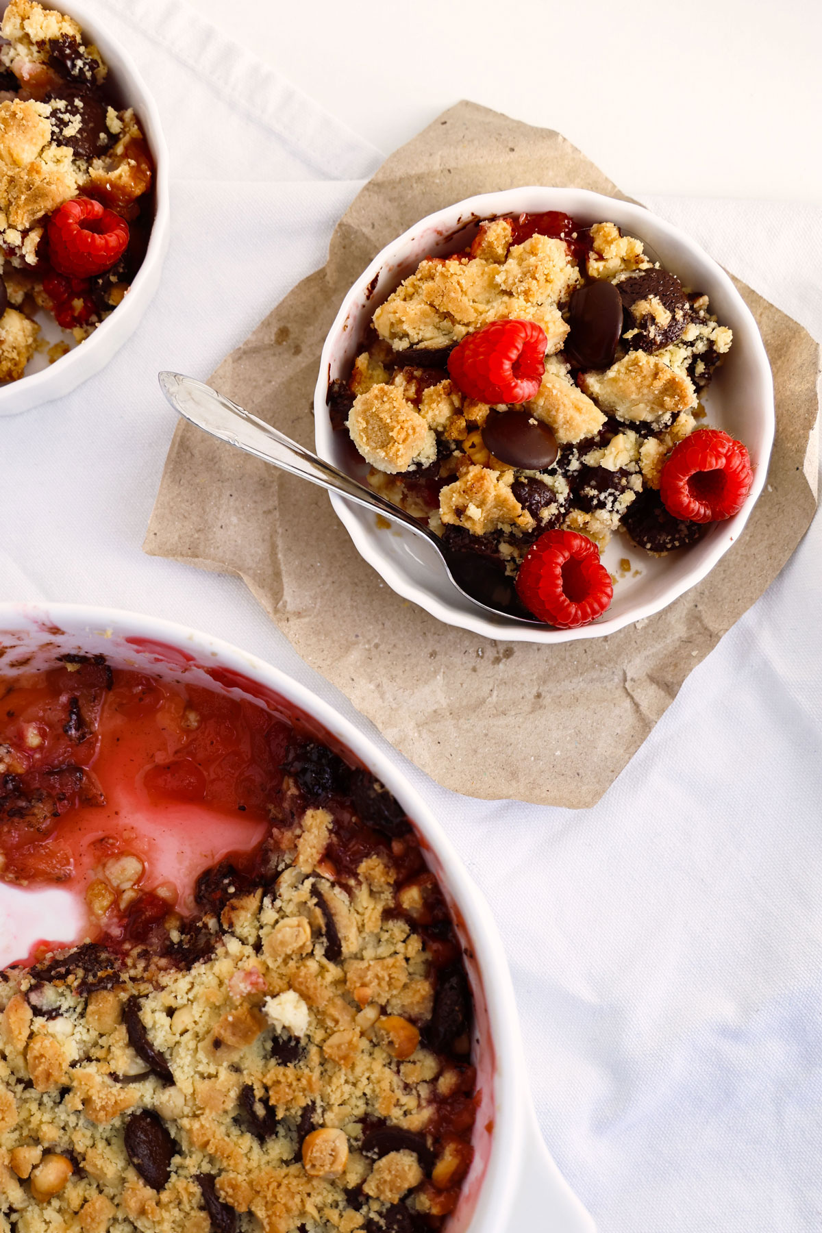 A portion of apple and raspberry crumble with chocolate chips and berries in a small white bowl.