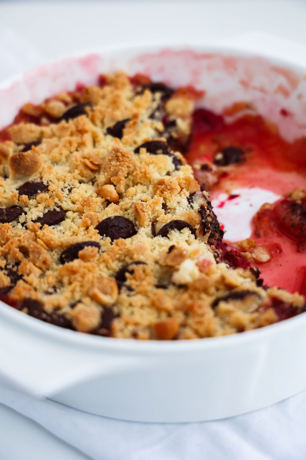 Baked apple and raspberry crumble with a golden crisp topping and read saucy fruit base in a white oven dish.