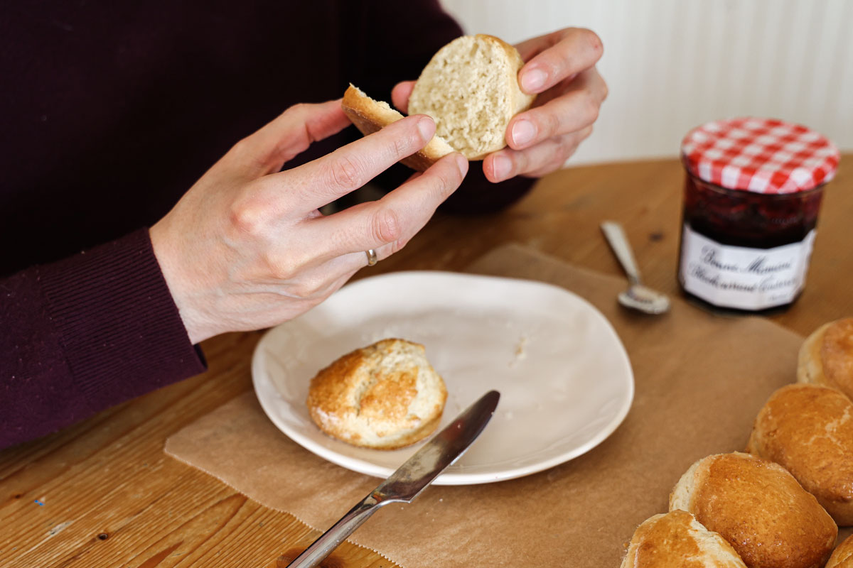 Hands opening a scone cut in half above a white plate.
