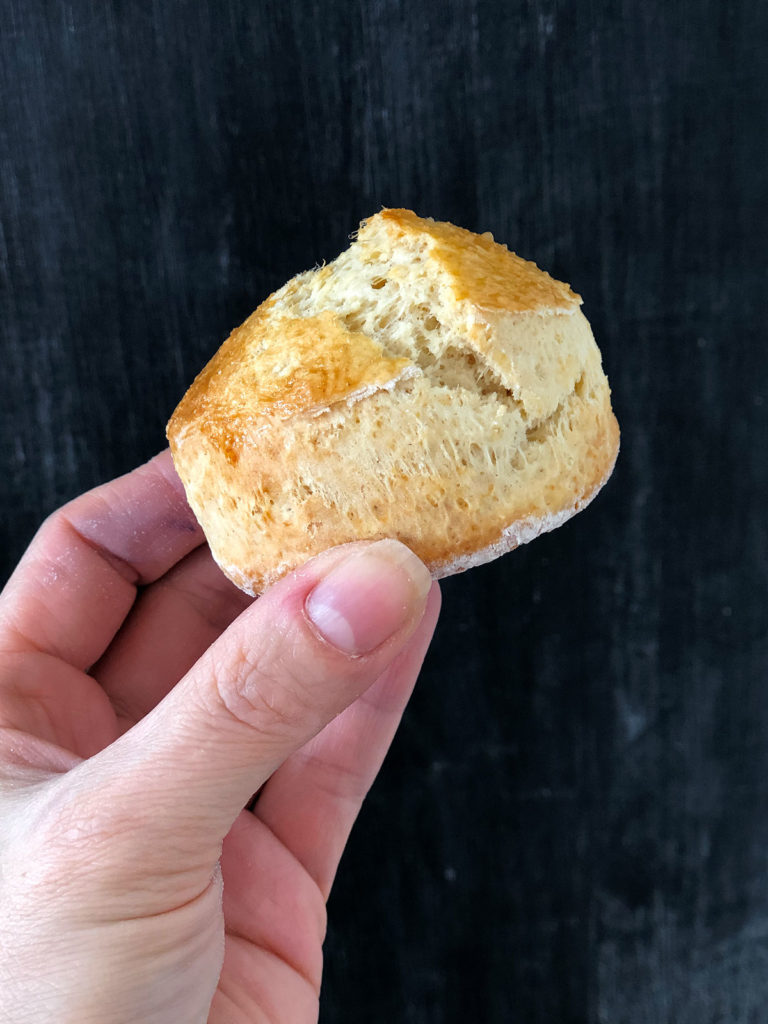 A hand holding a scone infront of black background.