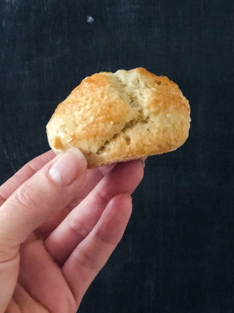 A hand holding a scone infront of black background.