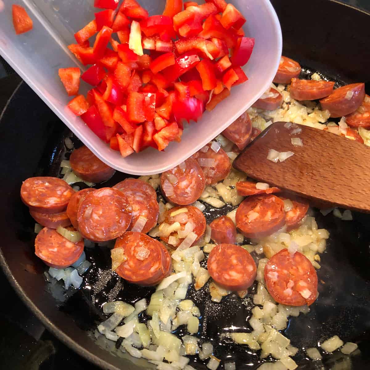 A picture of a recipe step - adding red paprika into the pan with chorizo and fried onion. 