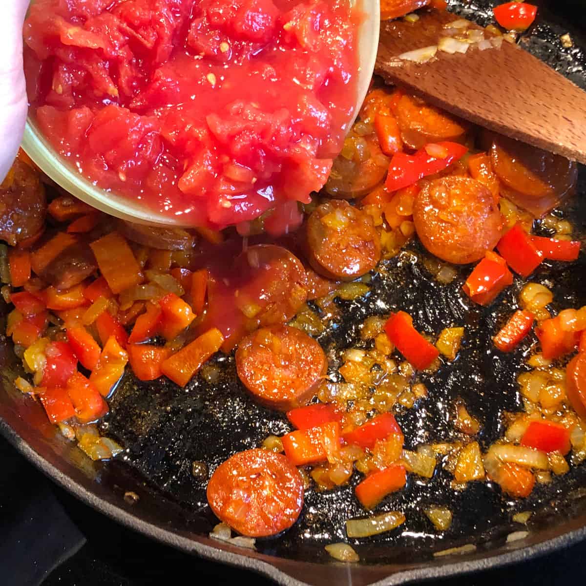 A picture of a recipe step - adding chopped tin tomatos into a fried ingredients. 