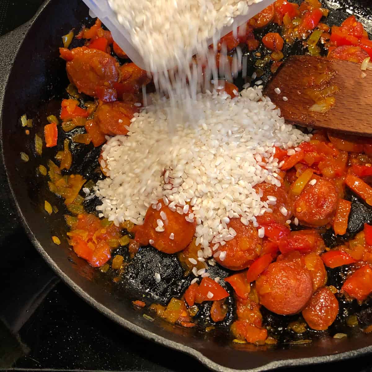 A picture of a recipe step - Adding paella rice into a soffrito. 