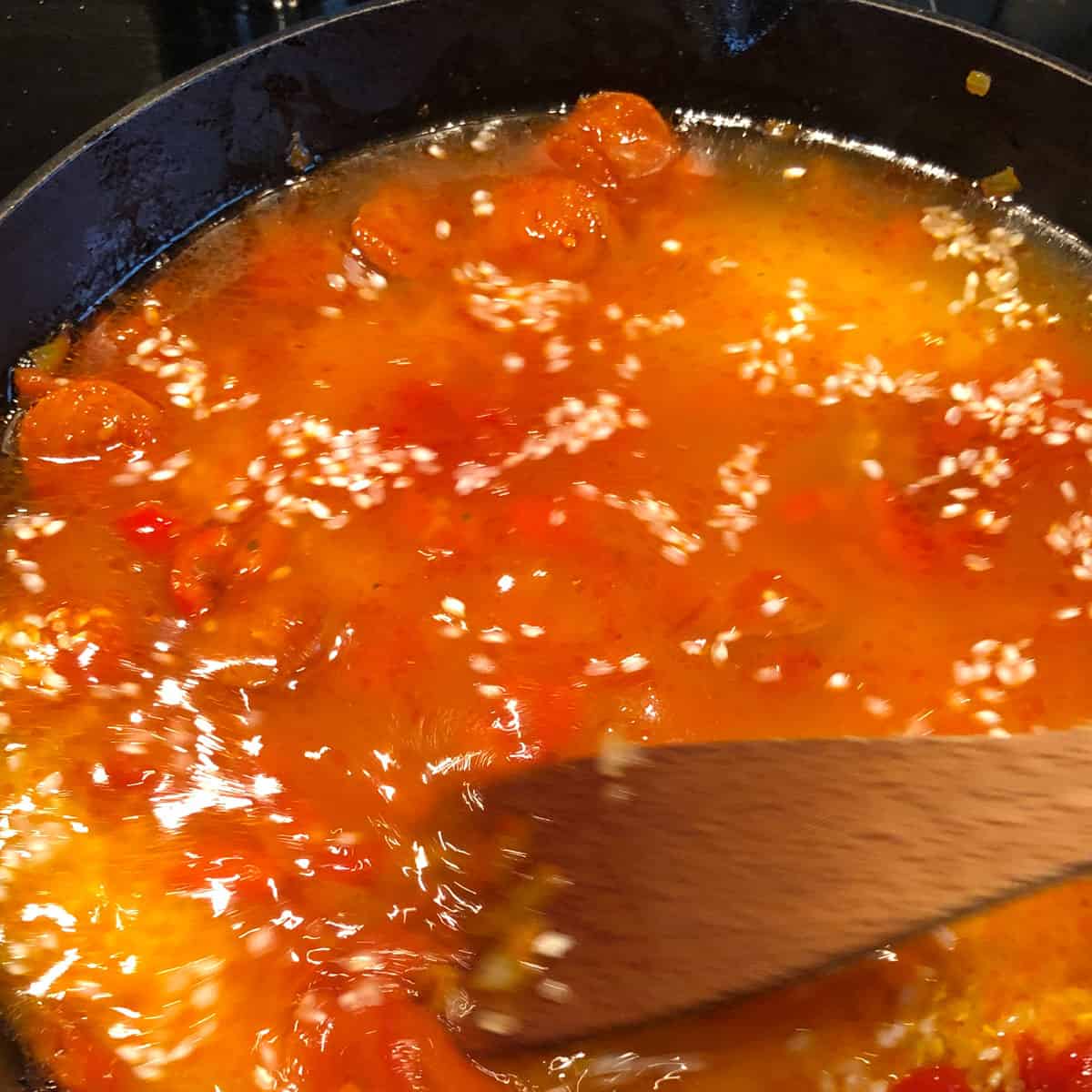 A picture of a recipe step - stock mixed with soffrito in a pan.