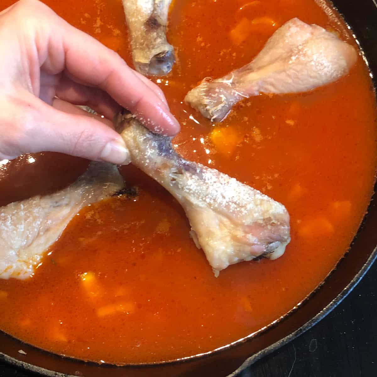 A picture of a recipe step - adding roasted chicken drumstick to a pan with paella ingredients.