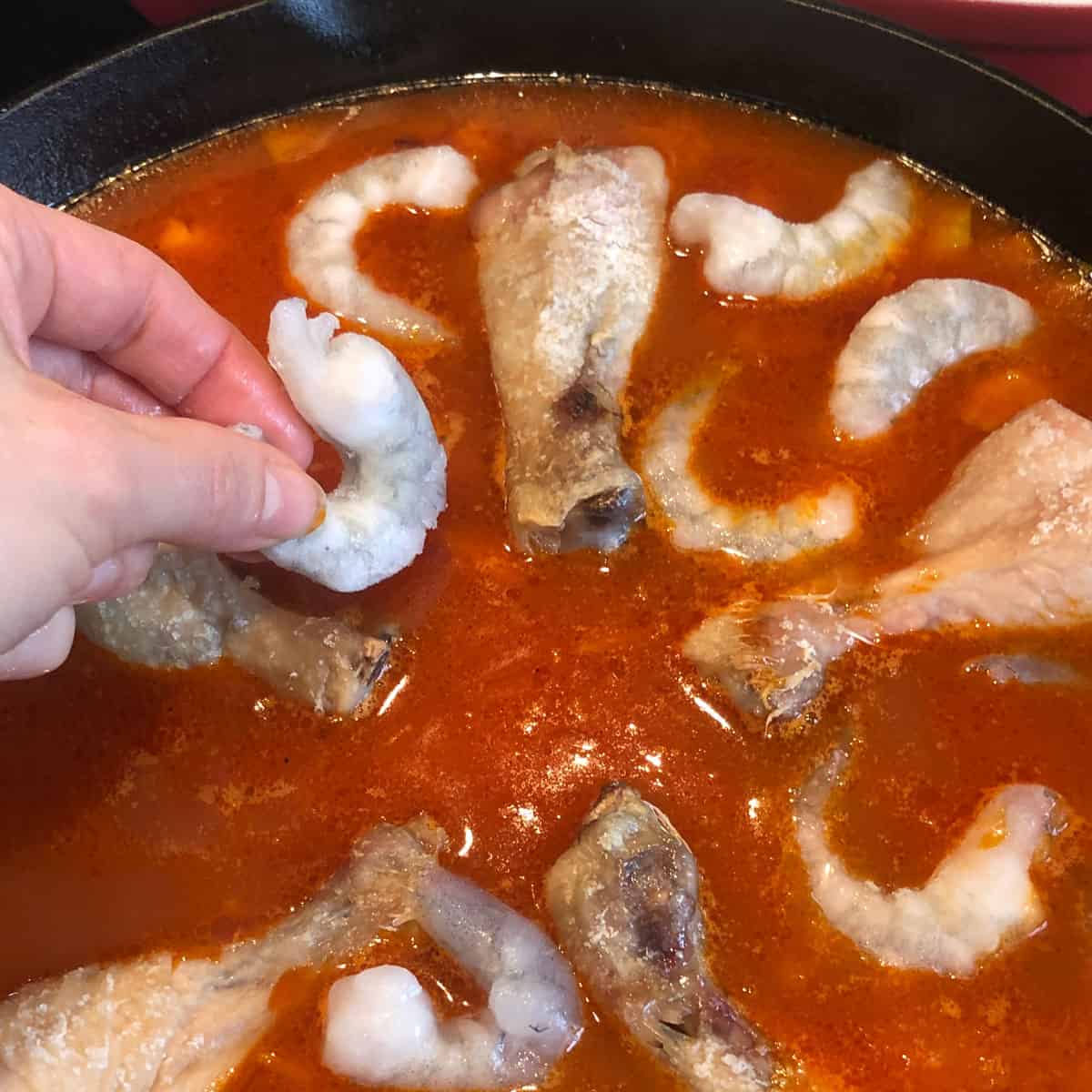 A picture of a recipe step - frozen raw king prawns to a pan with other paella ingredients.