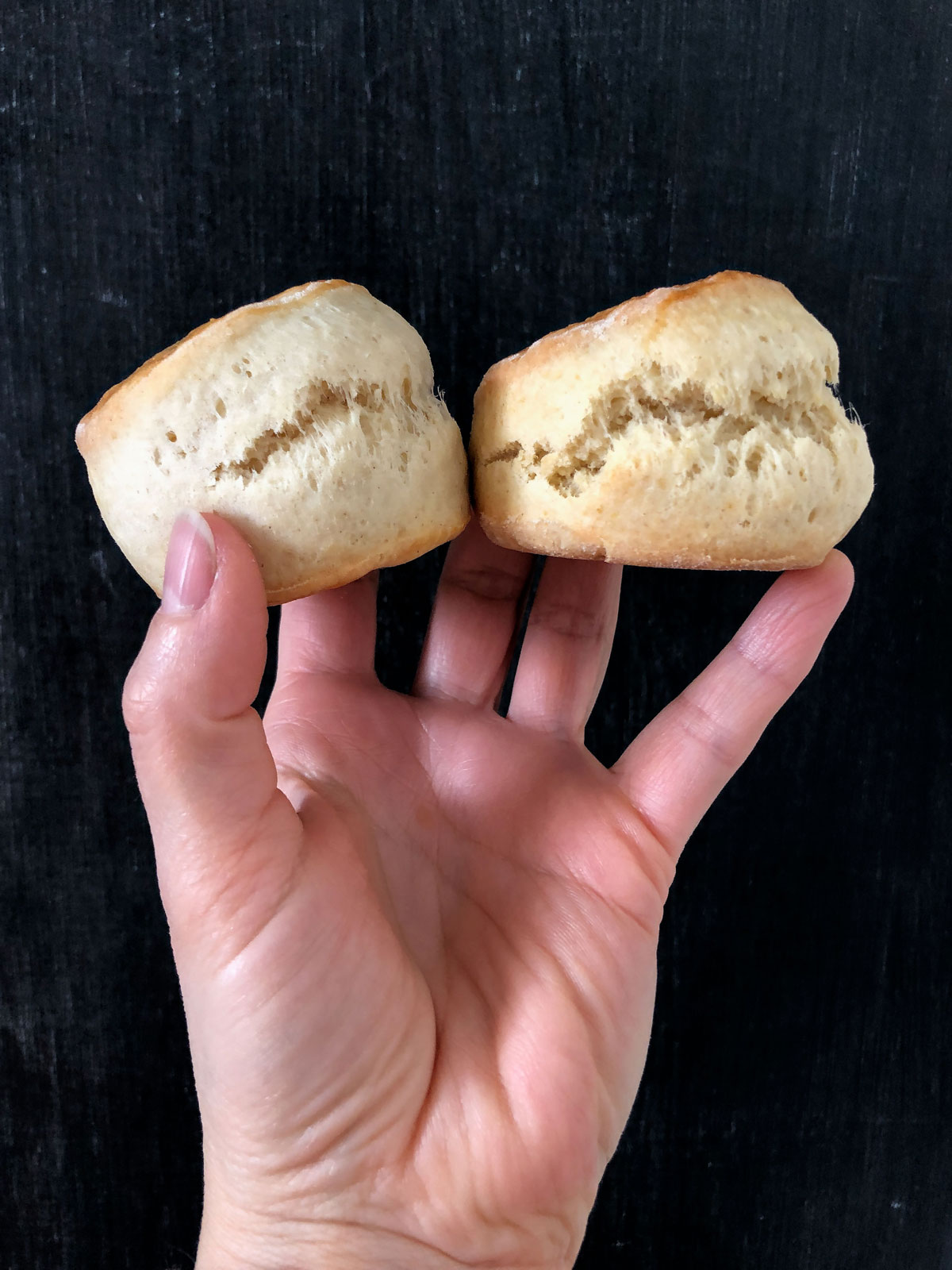 A hand holding two scones against black background.