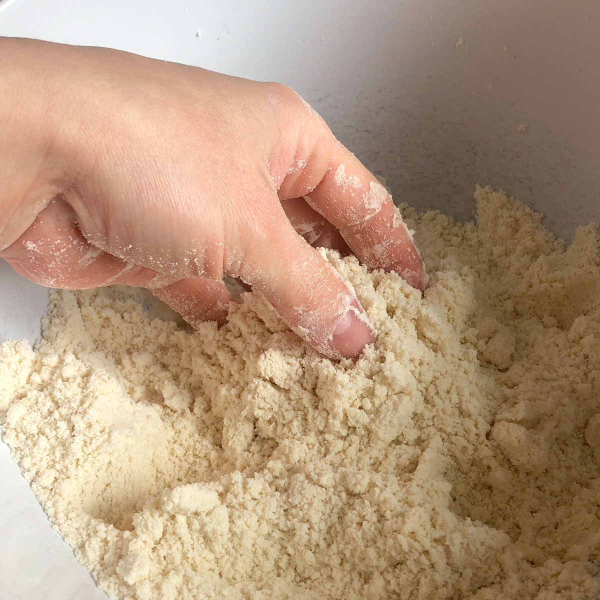 A hand rubbing butter into flour. 