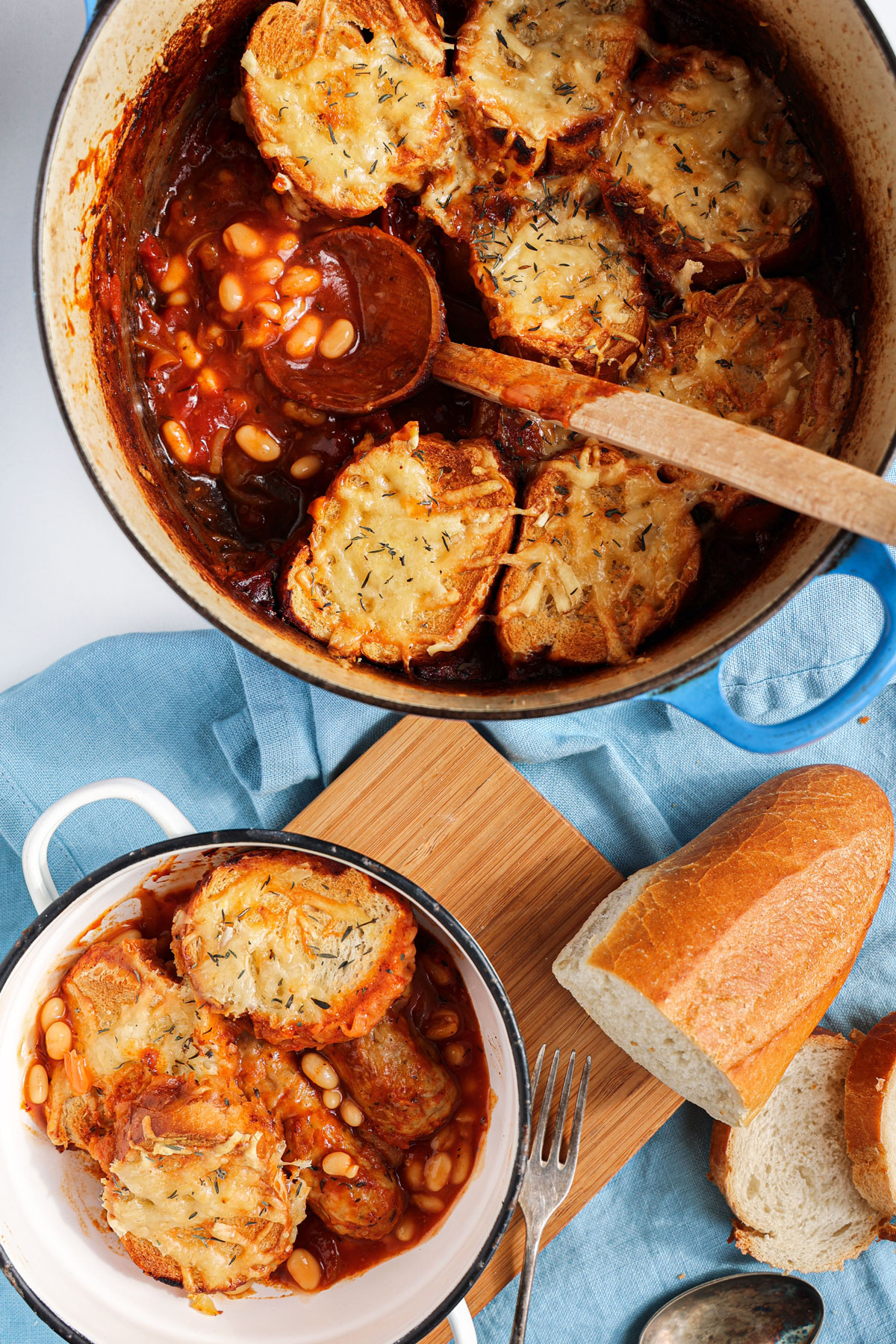 Sausage and bean hotpot with a cheesy baguetter in a cast-iron pot.