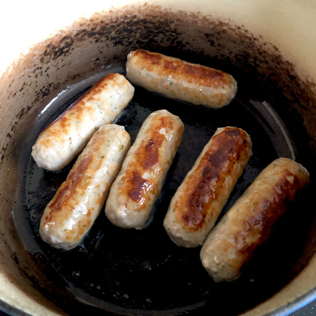 Browning sausages in a cast iron pot.