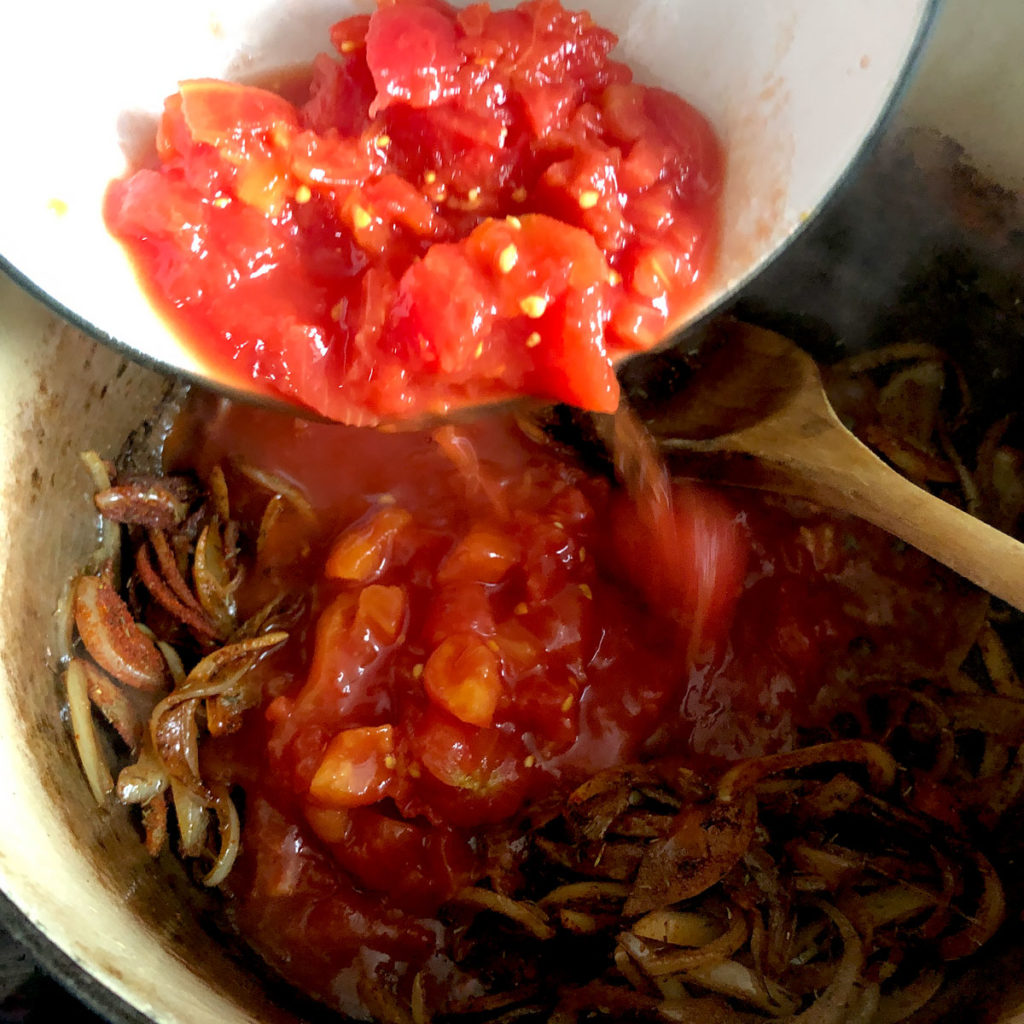 Adding chopped tomatoes into the pot with fried onion.