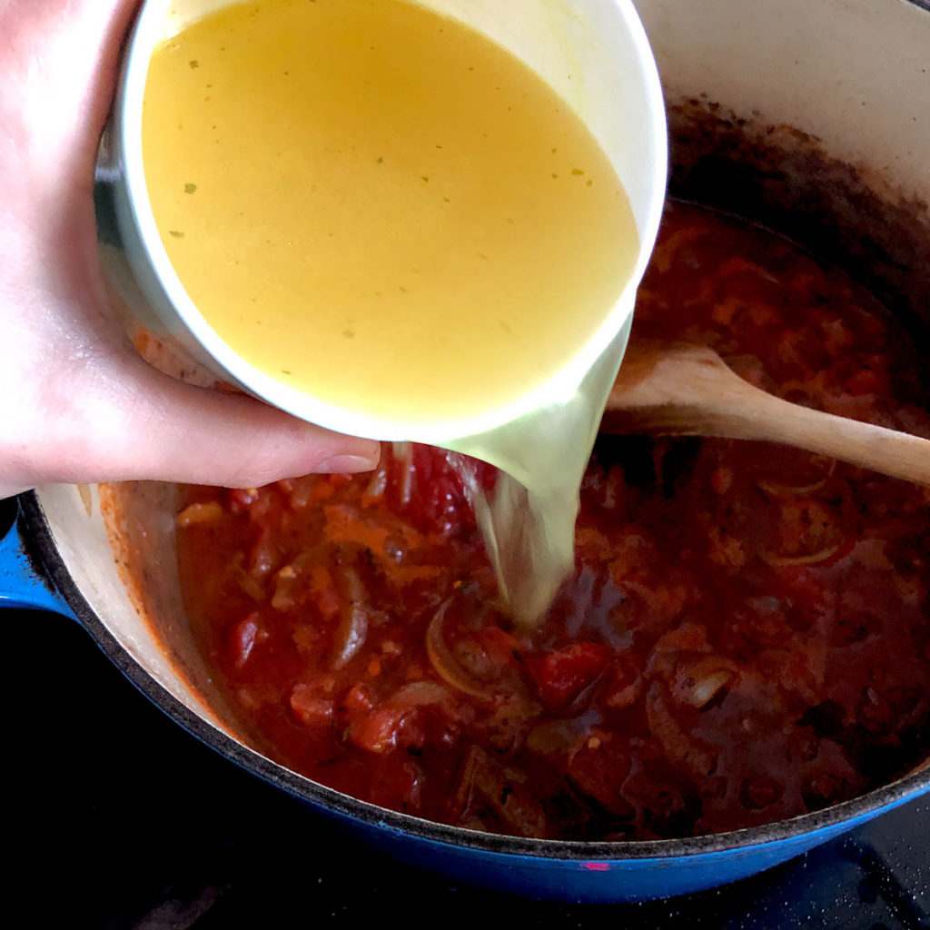 Pouring stock into a tomato sauce.