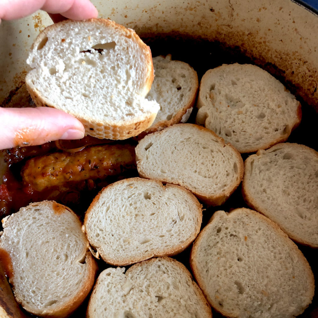 Arranging baguette slices on top of the sausages and red tomato sauce.