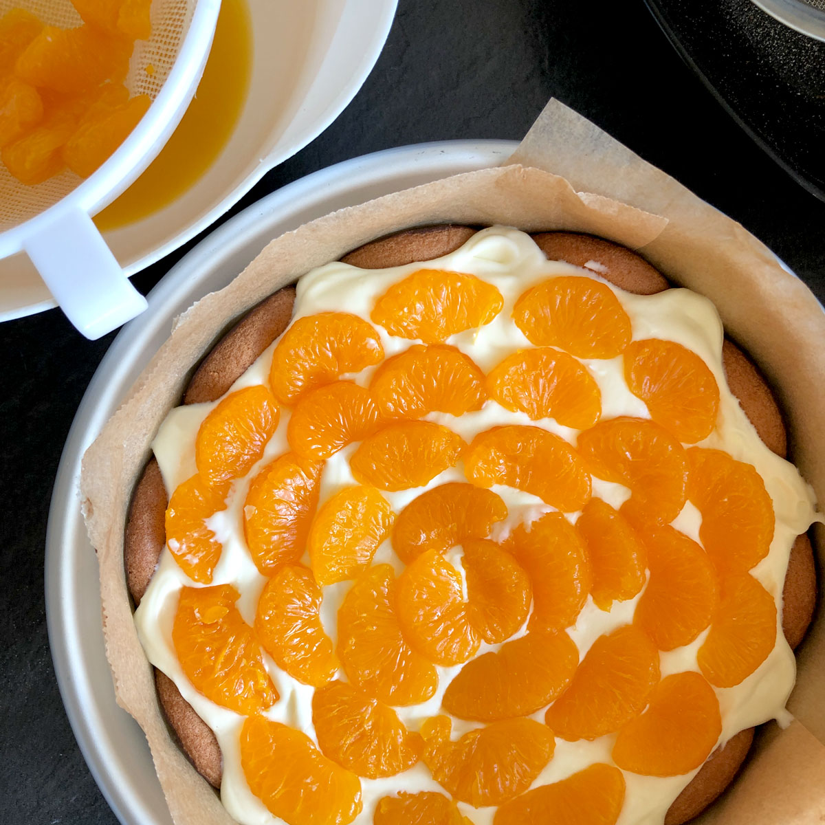 Tinned mandarins placed over whipped cream in a cake tin.