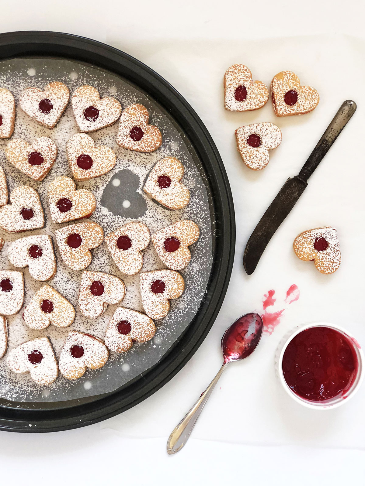 Jam sandwich biscuits filled with red jam on a tray.