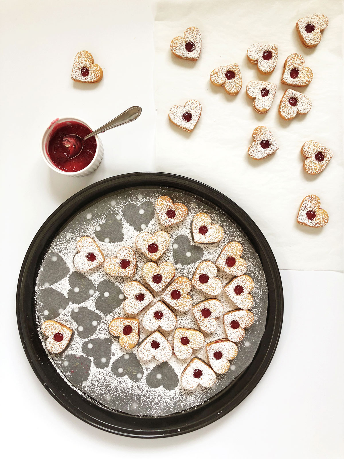 Small jam filled biscuits arranged on a round sheet with jam in a small bowl on the side.
