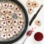 Heart shaped cookies on a tray filled with red jam.