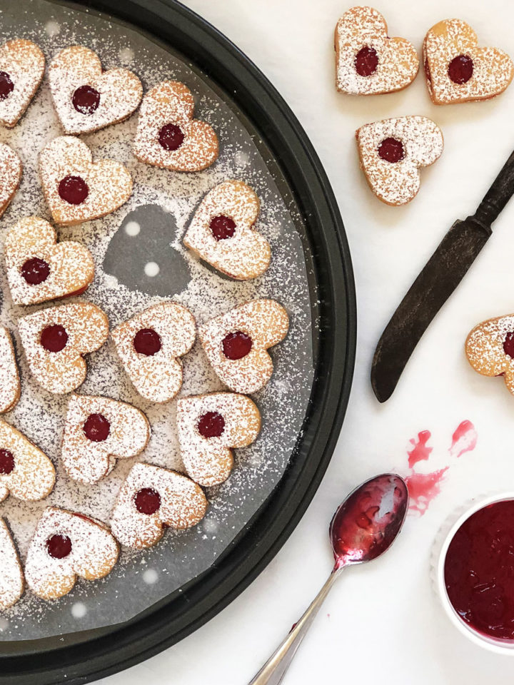 Heart shaped cookies on a tray filled with red jam.