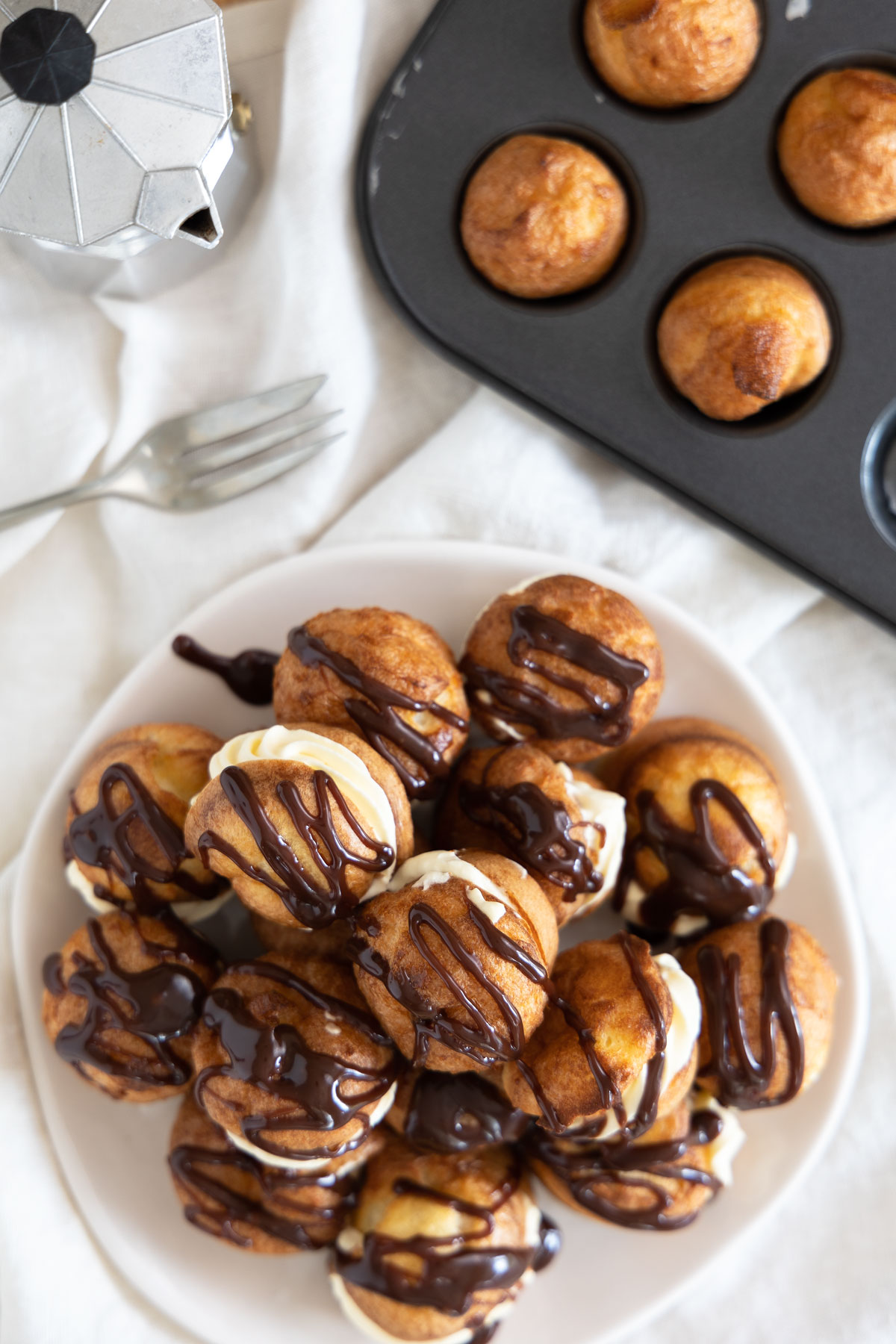 Sweet Yorkshire Puddings decorated like profiteroles on a white plate with a metal tray and a small caffetiere at the background.