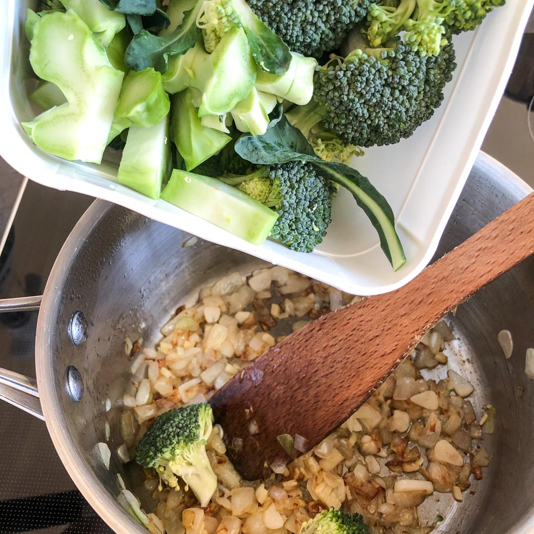 Tipping broccoli florets to a pot with caramelised onion.