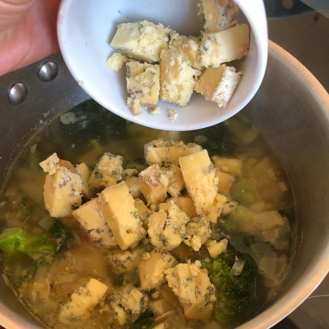 Adding cubbed stilton to broccoli soup.