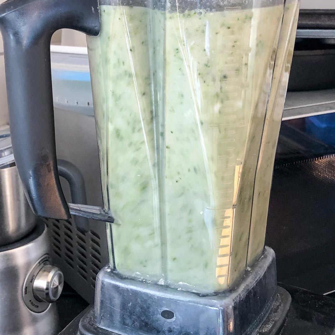 Blending broccoli soup in a stand blender.