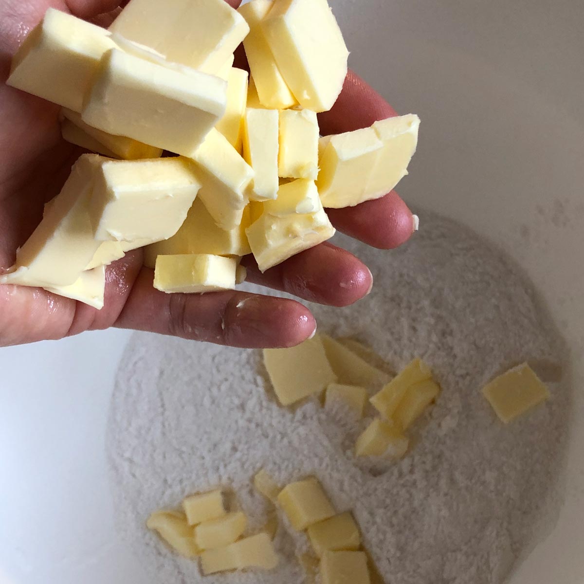 A hand carring cubbed butter into a bowl.