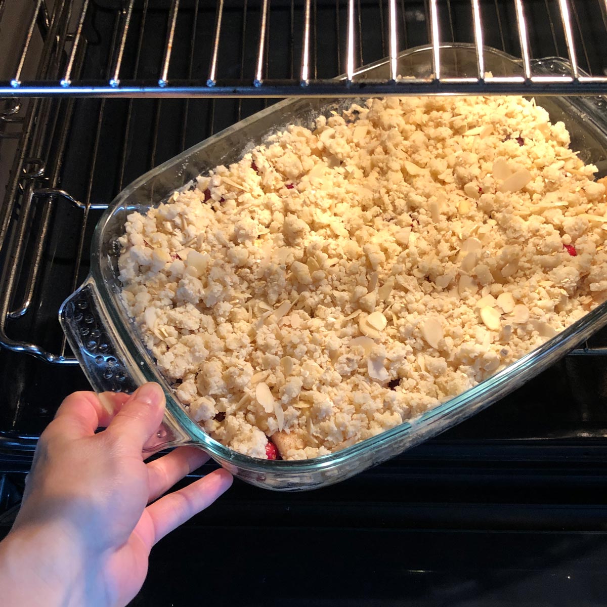 A glass baking dish with apple crumble being inserted into the oven.