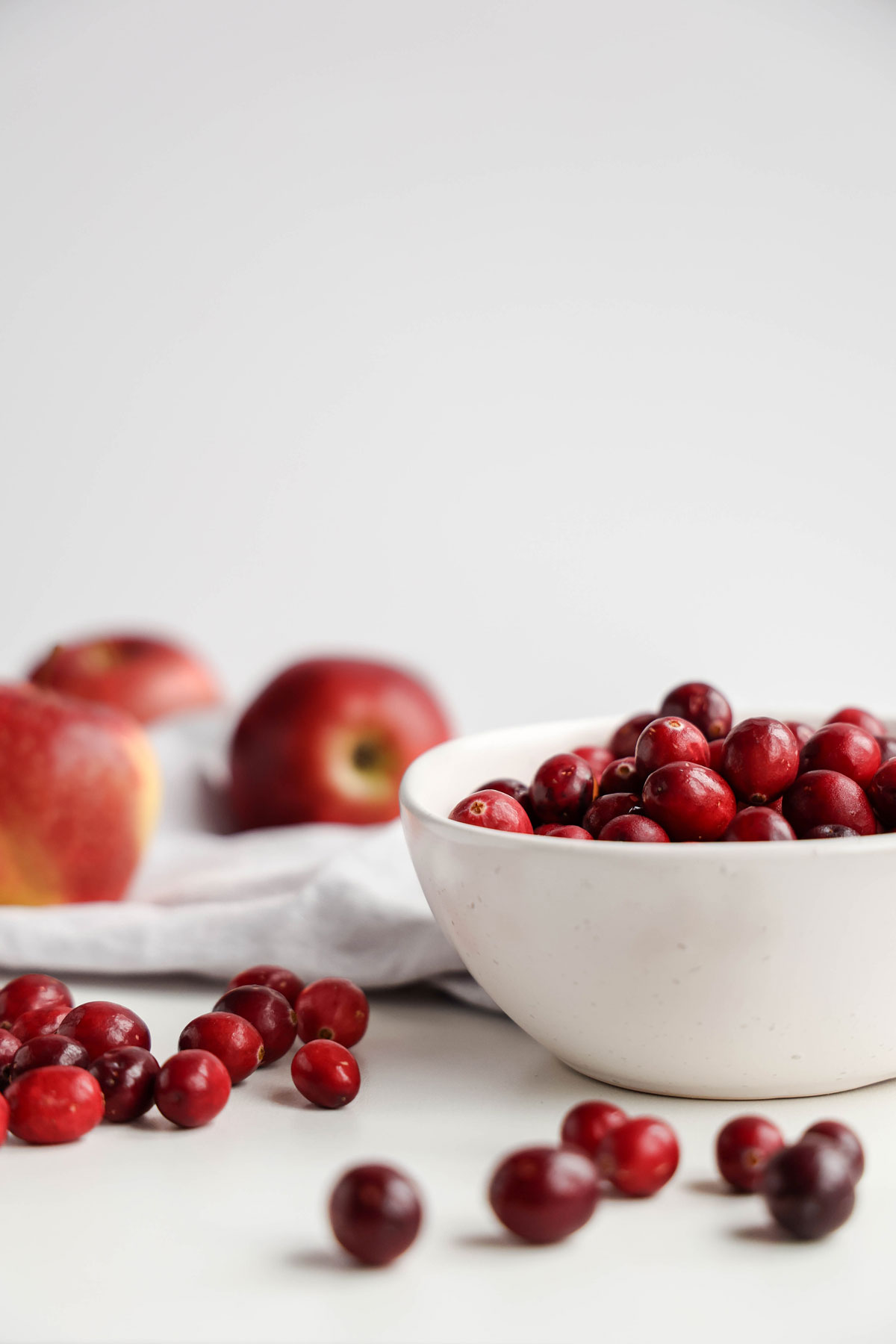 Fresh cranberries in a bowl with 3 apples at the background.