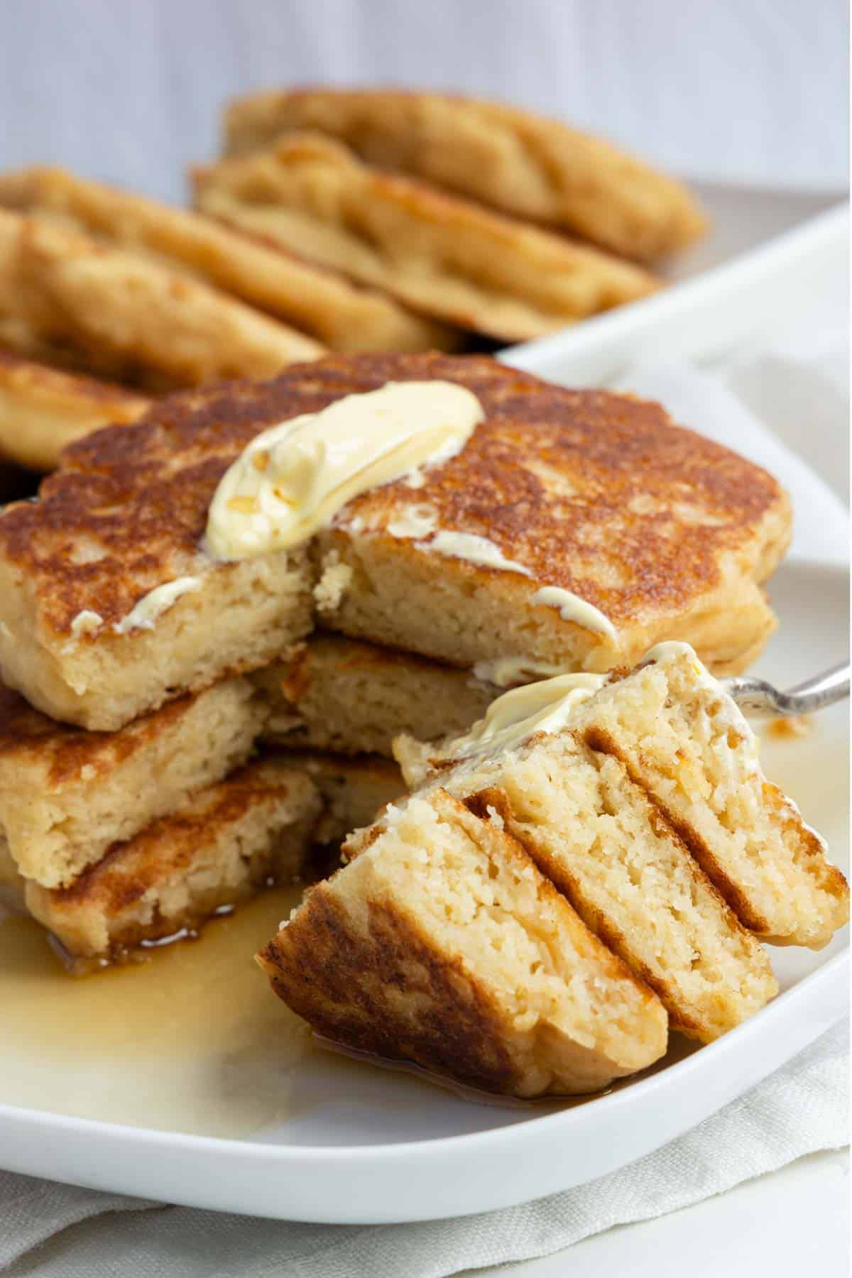 Three fluffy vegan pancakes in a stack on a plate with batter and maple syrup.