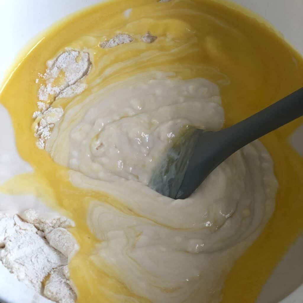 Mixing wet and dry ingredients for pancakes in a large white bowl.