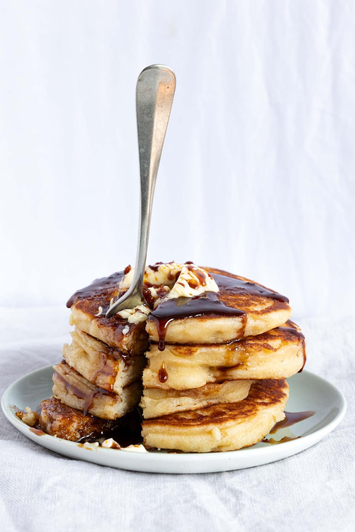 A stack of four fluffy pancakes with butter and syrup on a plate.