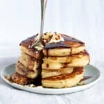 A stack of four fluffy pancakes with butter and syrup on a plate.