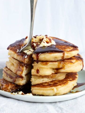 A stack of four fluffy pancakes with butter and syrup on a plate.