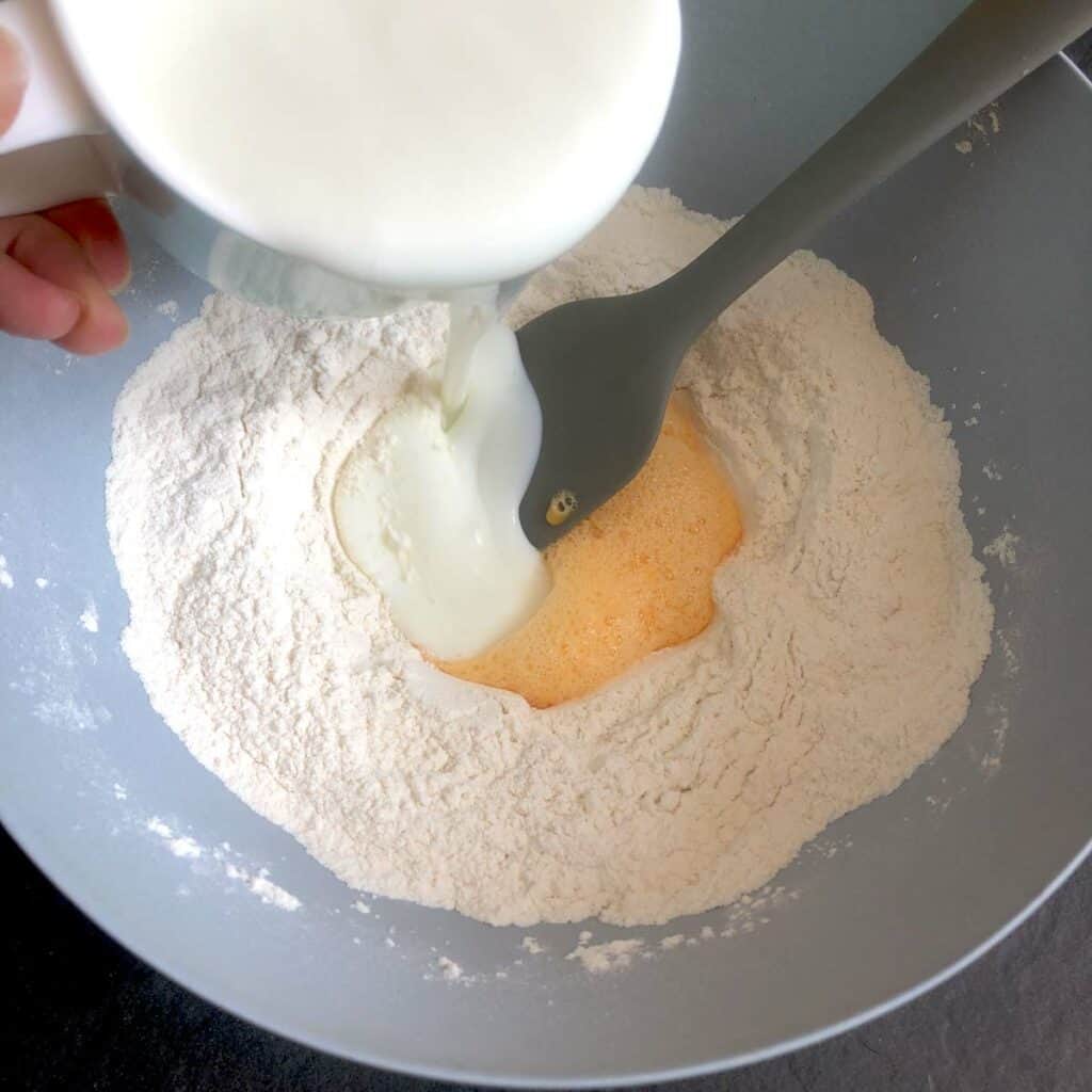 Pouring buttermilk into a bowl with flour and beaten egg.